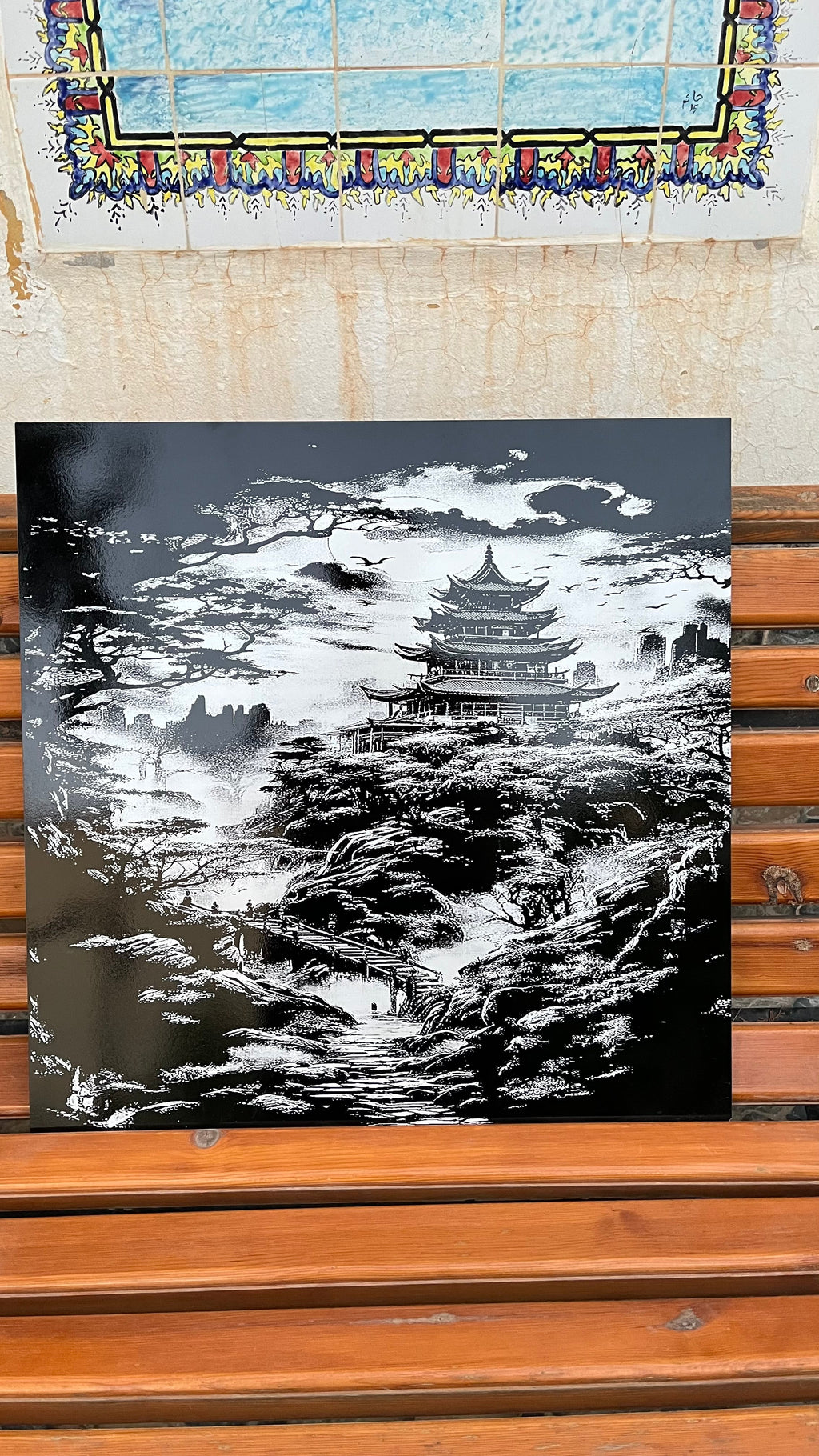 Tableau Temple Impérial en céramique gravée au laser, posé sur un banc en bois devant un mur en zellige