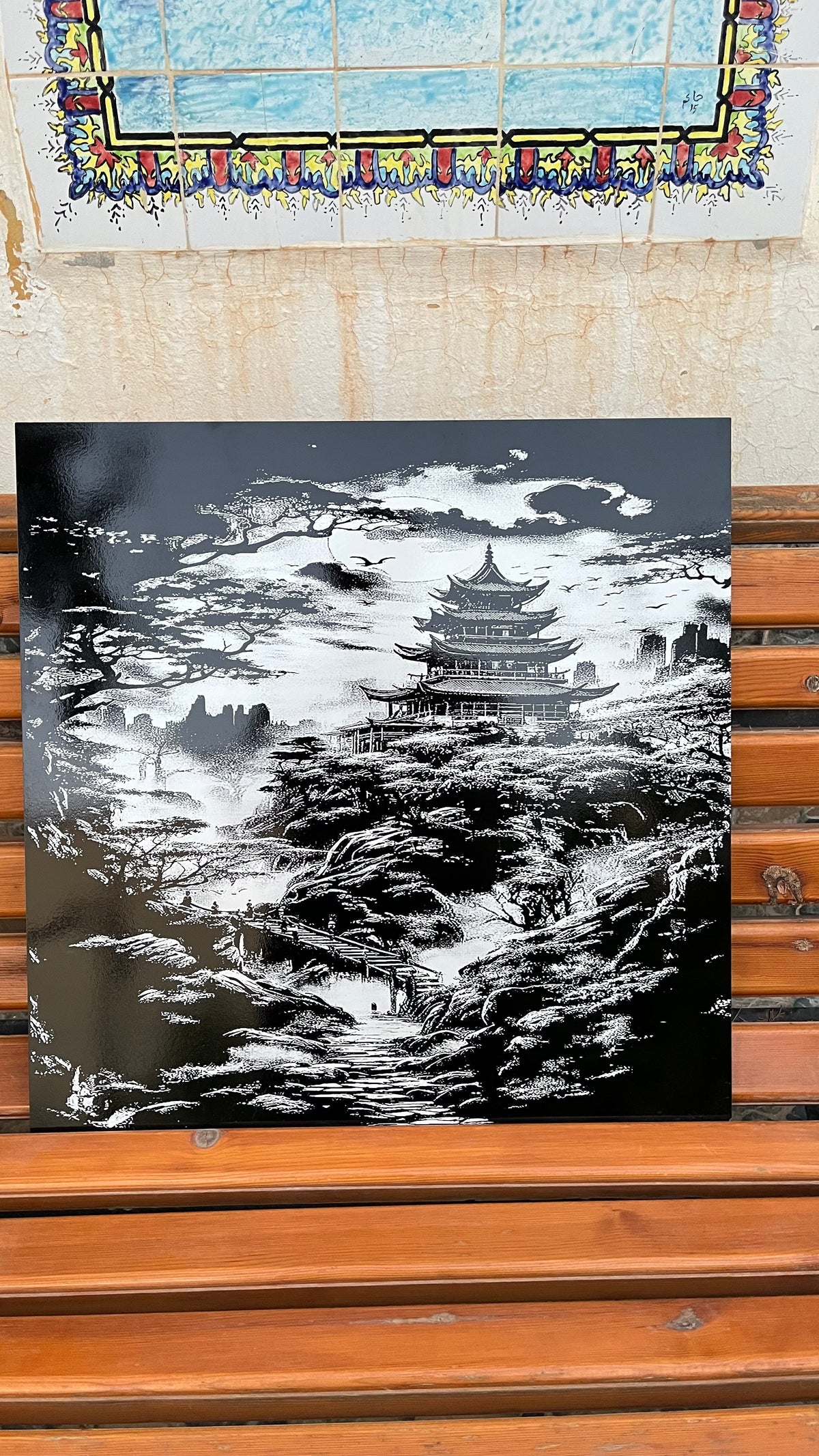 Tableau Temple Impérial en céramique gravée au laser, posé sur un banc en bois devant un mur en zellige